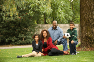 Family of 4 smiling on grass holding soccer ball
