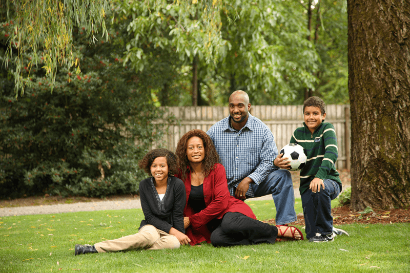 Family of 4 smiling on grass holding soccer ball